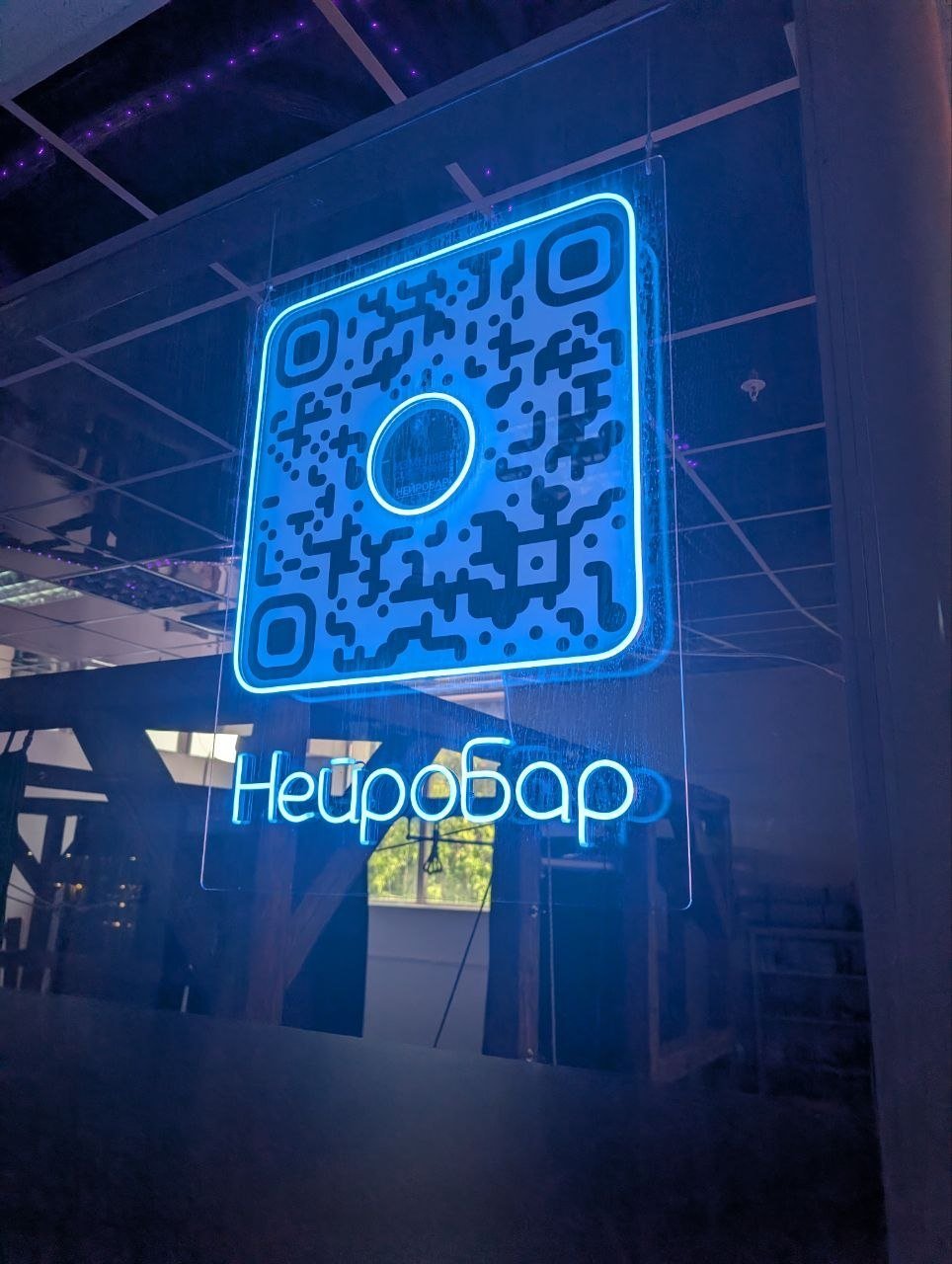 Неоновая вывеска «НейроБар» с голубым QR-кодом на прозрачной панели под потолком