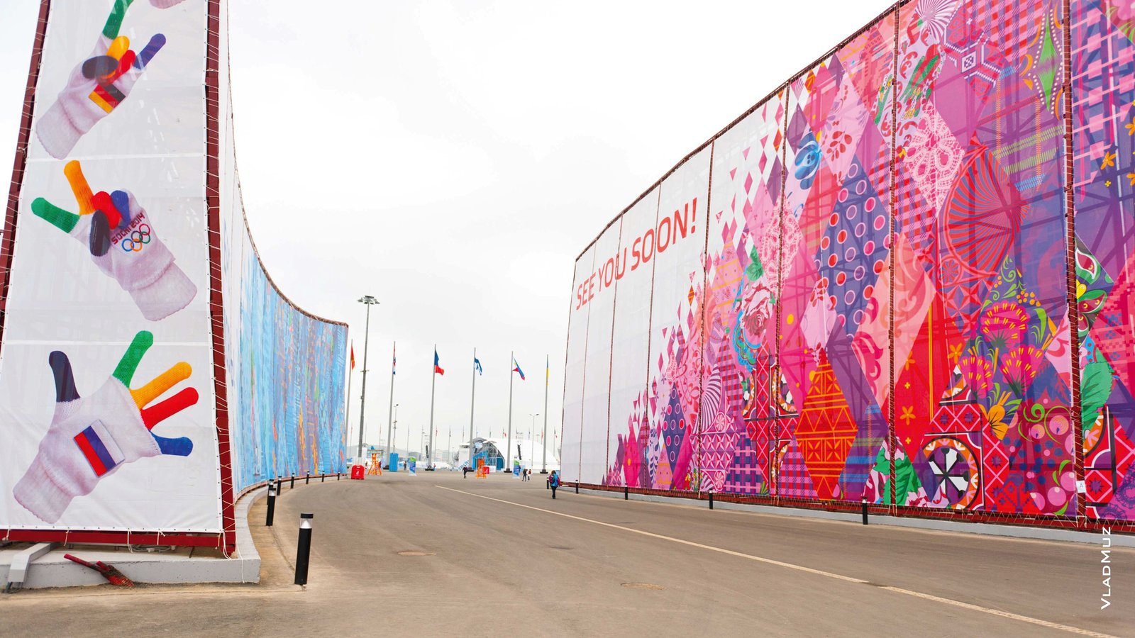 Баннерное оформление ограждений с символикой «Sochi 2014»: варежки с флагами на одной стене, надпись «See you soon!» на пёстром узоре — на другой